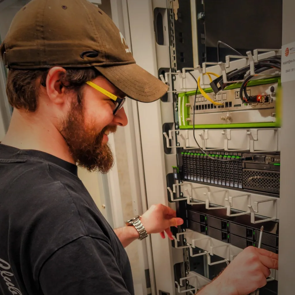 Techniker mit Cap und Brille bei der Arbeit am Serverschrank.