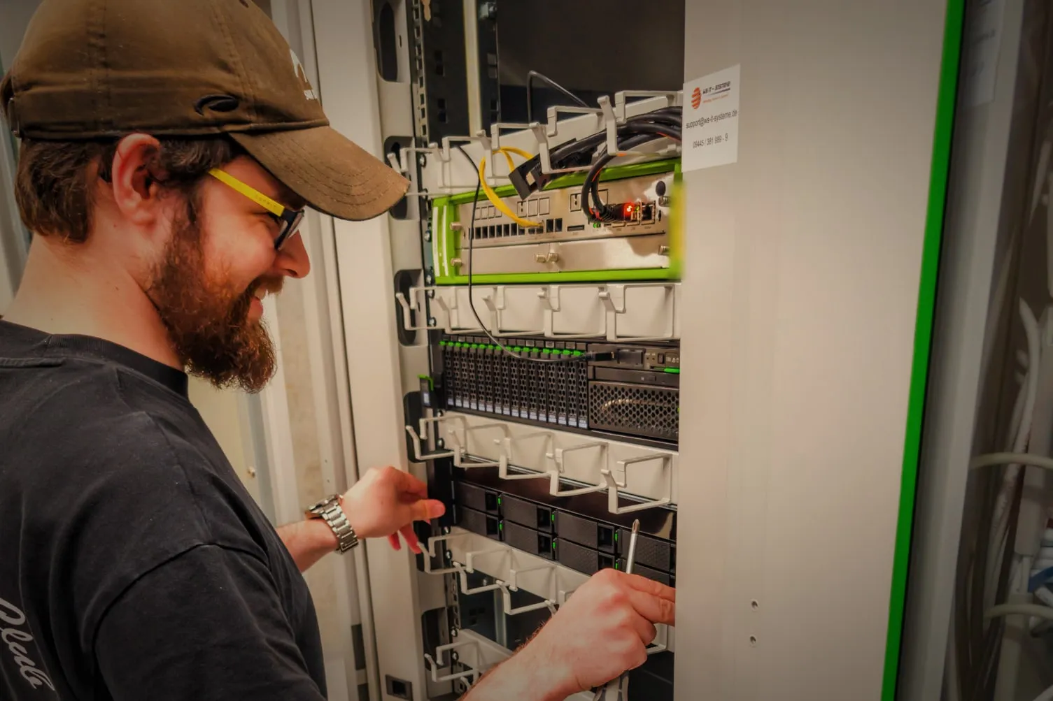 Techniker beim Einbau eines Geräts in den Serverschrank, mit Schraubendreher und geöffneter Schranktür.