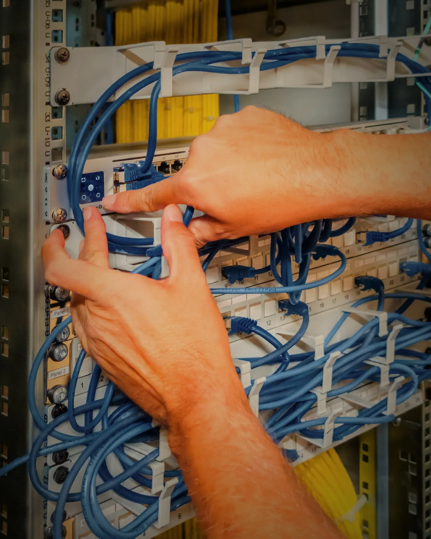 Zwei Hände stecken blaue Patchkabel am Patchfeld eines Netzwerkschranks